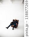 Man sits in a chair in a bright room with a simple background during a photoshoot 138877269