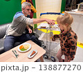 Man serves food to young girl at a table in a bright indoor space during evening hours 138877270