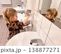 Young child washes hands in bathroom while looking in mirror 138877271
