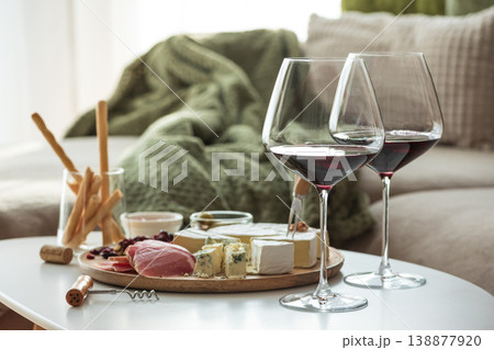 Cozy living room with two glasses of red wine and cheese on table 138877920