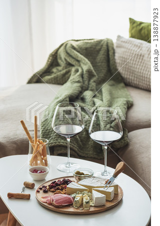 Wooden platter with assorted cheeses, cured meats, dried fruits, nuts and olives, accompanied by two glasses of red wine and lit candles against cozy sofa Wooden platter with assorted cheeses, cured meats, dried fruits, nuts and olives, accompanied by two glasses of red wine and lit candles against cozy sofa 138877923