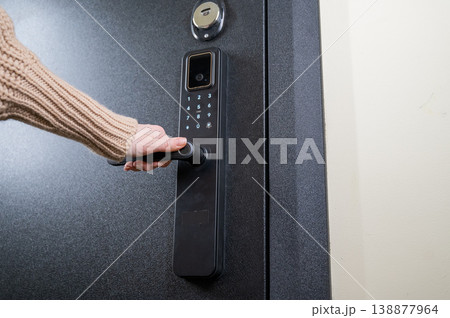 A woman opens a modern smart door lock with a digital keypad and biometric fingerprint access. A woman opens a modern smart door lock with a digital keypad and biometric fingerprint access. 138877964