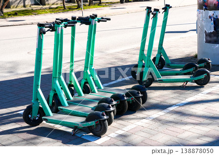 Row of shared electric scooters parked on city sidewalk ready for urban transport rental use 138878050