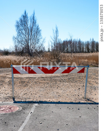 End of the road barrier with red and white stripes blocking access to gravel path in rural area 138878053