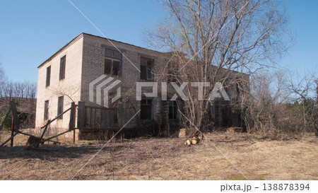 Abandoned Concrete Two Story Dormitory Near Trees, Boarded Windows, Stacked Logs, Ragged Entrance, Open Field, 138878394