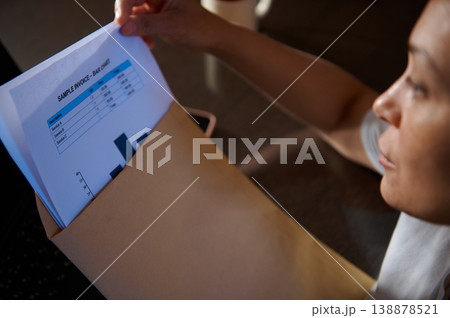 Woman Reviewing Sample Invoice and Bar Chart Pulled From Folder in Office Workspace 138878521
