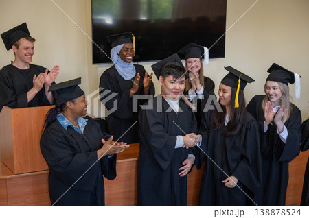 Young multinational people in graduation gowns congratulate each other on graduation from university.  138878524