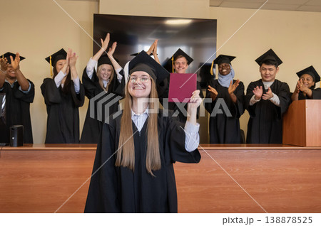 Happy Caucasian woman holds red diploma and classmates support her.  138878525