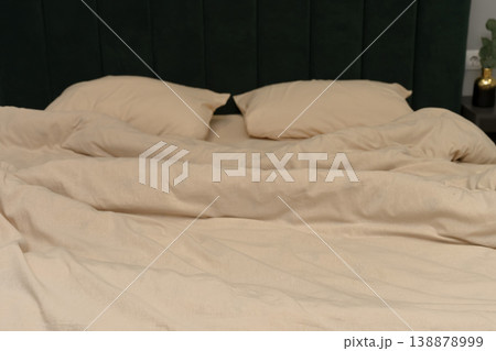 Cozy beige bedding with two pillows on a green upholstered headboard 138878999