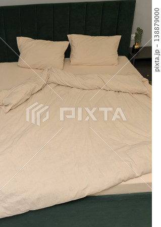 Neatly made bed with beige bedding and green upholstered headboard Neatly made bed with beige bedding and green upholstered headboard 138879000