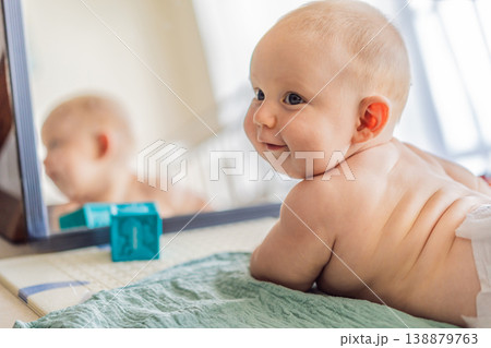 Baby lying on play mat learning to crawl and get on all fours. Infant practicing motor skills and development at home. Early childhood growth, milestones and active learning concept 138879763