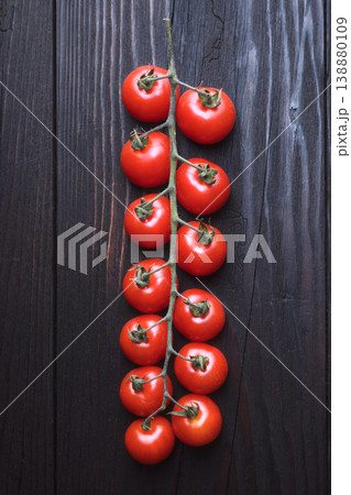 Vertical composition of cherry tomatoes on vine against dark wooden background Vertical composition of cherry tomatoes on vine against dark wooden background 138880109