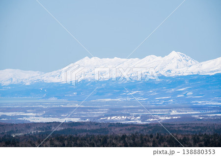冬の平原越しに見える遠方の雪山連峰。北海道の大自然を代表する絶景。白銀に輝く山頂と澄み渡る青空の冬の 138880353