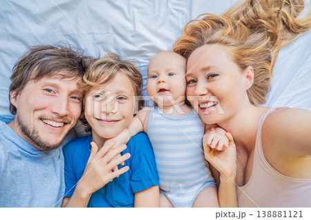 Baby lying on bed with mother, father and older brother at home. Happy family spending time together, bonding and relaxing. Parenthood, sibling connection and warm family life concept 138881121