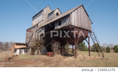 Derelict Wooden Grain Elevator On Stilts Towers Over Empty Field Under Clear Sky. Rusted Corrugated Metal Derelict Wooden Grain Elevator On Stilts Towers Over Empty Field Under Clear Sky. Rusted Corrugated Metal 138881270