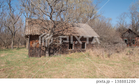 Abandoned Wooden Farmhouse In Belarus Sits Amid Overgrown Meadow Under Clear Blue Sky. Leafless Trees Press Abandoned Wooden Farmhouse In Belarus Sits Amid Overgrown Meadow Under Clear Blue Sky. Leafless Trees Press 138881280