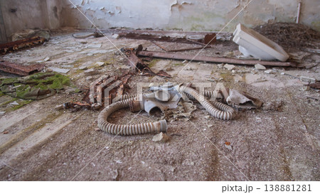 Gas Mask Abandoned On Cracked Floor, Discarded Decontamination Gear With Coiled Hoses, Peeling Plaster, Moss 138881281