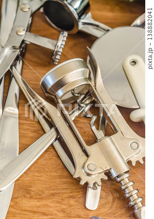 A pile of essential shiny metal kitchen gadgets like a wine opener, pizza cutter, and shears lying on a wooden kitchen counter.. High quality photo A pile of essential shiny metal kitchen gadgets like a wine opener, pizza cutter, and shears lying on a wooden kitchen counter.. High quality photo 138882041