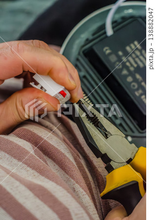 Close-up of a person's hands holding yellow pliers and a white electrical terminal connector during an LED light fixture installation.. High quality photo 138882047