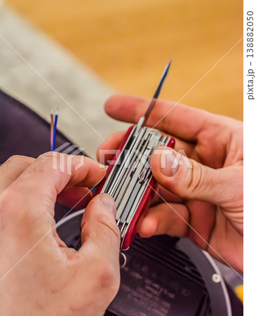 Close up of a handyman using a versatile red multitool to strip electrical wires. DIY home improvement and repair project. High quality photo 138882050