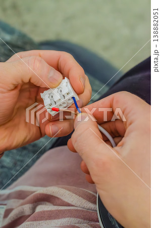 Close-up of male hands carefully connecting brown and blue electrical wires into a white plastic terminal block during home renovation work.. High quality photo Close-up of male hands carefully connecting brown and blue electrical wires into a white plastic terminal block during home renovation work.. High quality photo 138882051