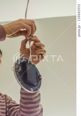 An electrician connects the electrical wires for a modern, energy-efficient recessed ceiling light. Home improvement and repair.. High quality photo An electrician connects the electrical wires for a modern, energy-efficient recessed ceiling light. Home improvement and repair.. High quality photo 138882052
