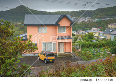 Muroran, Hokkaido, Japan - Oct 4 2024, panoramic view of a two-storey peach-colored private house with a parked off-road car at porch, with mountains on background, in cloudy weather, Muroran, Japan 138882136
