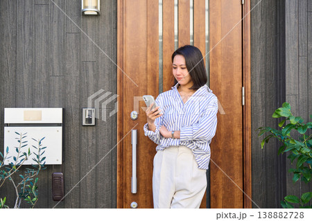 一軒家の玄関前でスマホで通話しながら笑顔を見せる外出前の日本人女性 一軒家の玄関前でスマホで通話しながら笑顔を見せる外出前の日本人女性 138882728