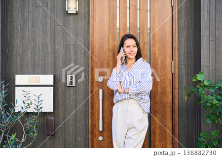 一軒家の玄関前でスマホで通話しながら笑顔を見せる外出前の日本人女性 一軒家の玄関前でスマホで通話しながら笑顔を見せる外出前の日本人女性 138882730