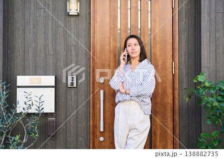 一軒家の玄関前でスマホで通話しながら笑顔を見せる外出前の日本人女性 138882735