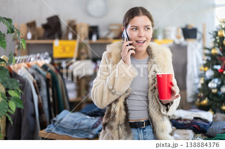 European girl with cup of coffee talking on phone in womens clothing store 138884376