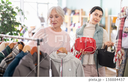Senior female client chooses jacket, assistant consultant offers purchase bag Senior female client chooses jacket, assistant consultant offers purchase bag 138884437