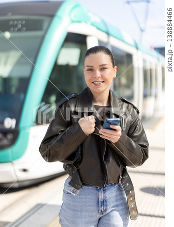 Young woman waiting for tram at stop with mobile phone Young woman waiting for tram at stop with mobile phone 138884466