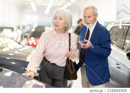 Senior salesman at car dealership offers to buy car to an elderly woman - demonstrating the best models of car dealership Senior salesman at car dealership offers to buy car to an elderly woman - demonstrating the best models of car dealership 138884569