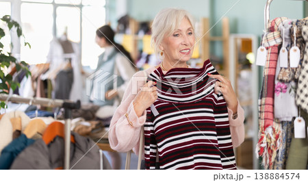 Mature woman choosing a warm knitted sweater in the store Mature woman choosing a warm knitted sweater in the store 138884574