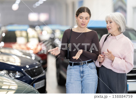 Adult daughter helps her elderly mother choose a new car at car dealership. Adult daughter helps her elderly mother choose a new car at car dealership. 138884759