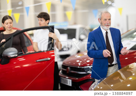 Elderly salesman selling car to young couple at dealership 138884897