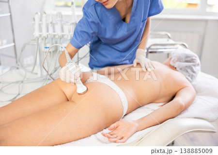 Young female cosmetologist performing ultrasound procedure on buttocks of young woman Young female cosmetologist performing ultrasound procedure on buttocks of young woman 138885009