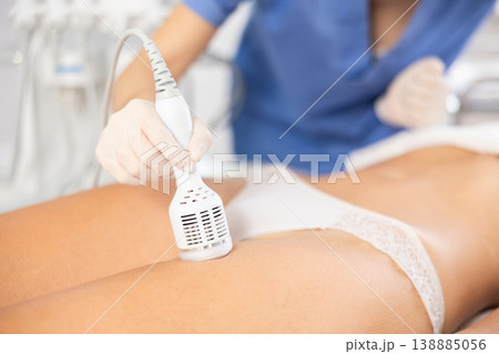 Aesthetician performing cryotherapy using cooling attachment on female client thighs 138885056