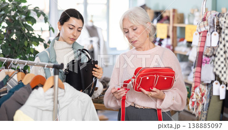 Elderly mother and her adult daughter choose together fashionable handbags in clothing store Elderly mother and her adult daughter choose together fashionable handbags in clothing store 138885097
