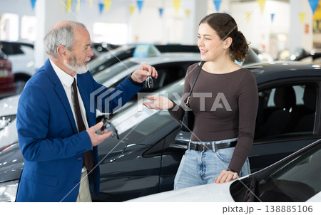 Elderly salesman selling car to young woman at dealership Elderly salesman selling car to young woman at dealership 138885106