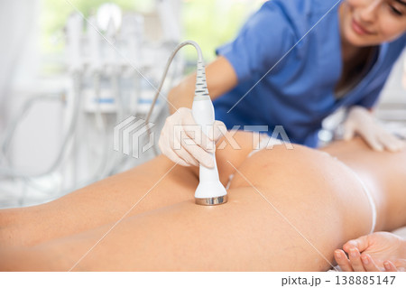 Cosmetologist performing high-frequency ultrasound procedure on female buttocks 138885147