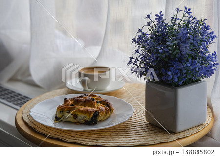 Enjoying coffee and croissant near a window with flowers in a cozy setting Enjoying coffee and croissant near a window with flowers in a cozy setting 138885802