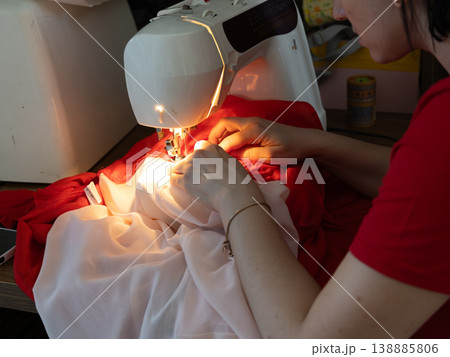 Lviv Ukraine 03.21.26 Woman sewing a shirt at a tabletop with a sewing machine in a workspace Lviv Ukraine 03.21.26 Woman sewing a shirt at a tabletop with a sewing machine in a workspace 138885806