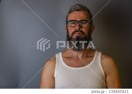 Man with beard wearing tank top stands against simple background Man with beard wearing tank top stands against simple background 138885821