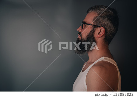 Man with beard is standing in profile against a plain wall Man with beard is standing in profile against a plain wall 138885822