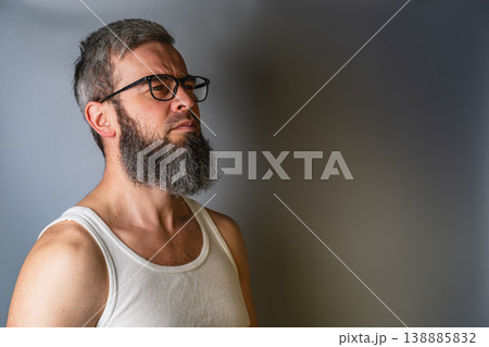 Man with beard stands against a gray wall wearing a tank top Man with beard stands against a gray wall wearing a tank top 138885832