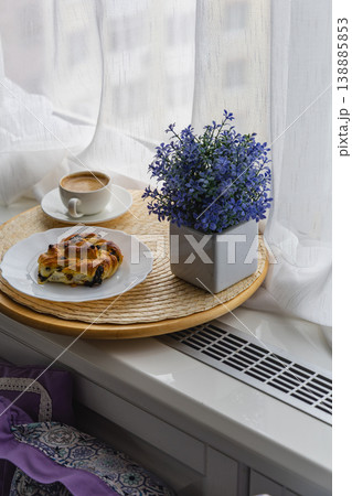 Coffee and pastry on a tray near a window with a flower pot Coffee and pastry on a tray near a window with a flower pot 138885853