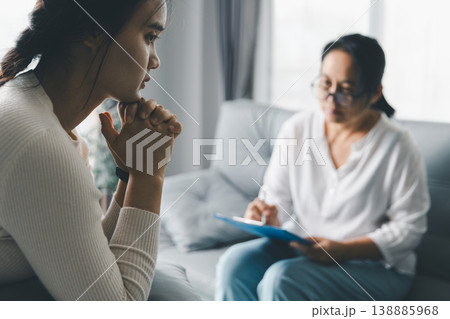 Mental health counseling concept with anxious woman in deep thought during therapy session while therapist takes notes, showing stress, reflection, trust, psychological support, and care. Mental health counseling concept with anxious woman in deep thought during therapy session while therapist takes notes, showing stress, reflection, trust, psychological support, and care. 138885968