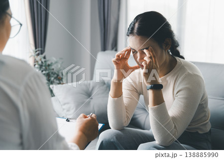 Mental health counseling concept with stressed woman touching temples during therapy session at home, showing anxiety, emotional pressure, therapist support, coping, trust and psychological care. 138885990
